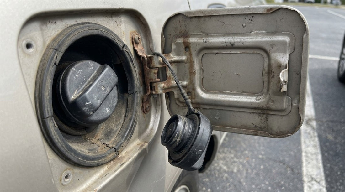 Tapa del tanque de gasolina abierta con el tapón colgando de su cordel y la goma del sello desgastada